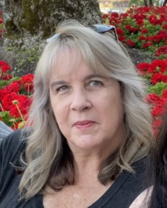 Woman in a dark grey shirt sitting in front of a bed of red flowers.